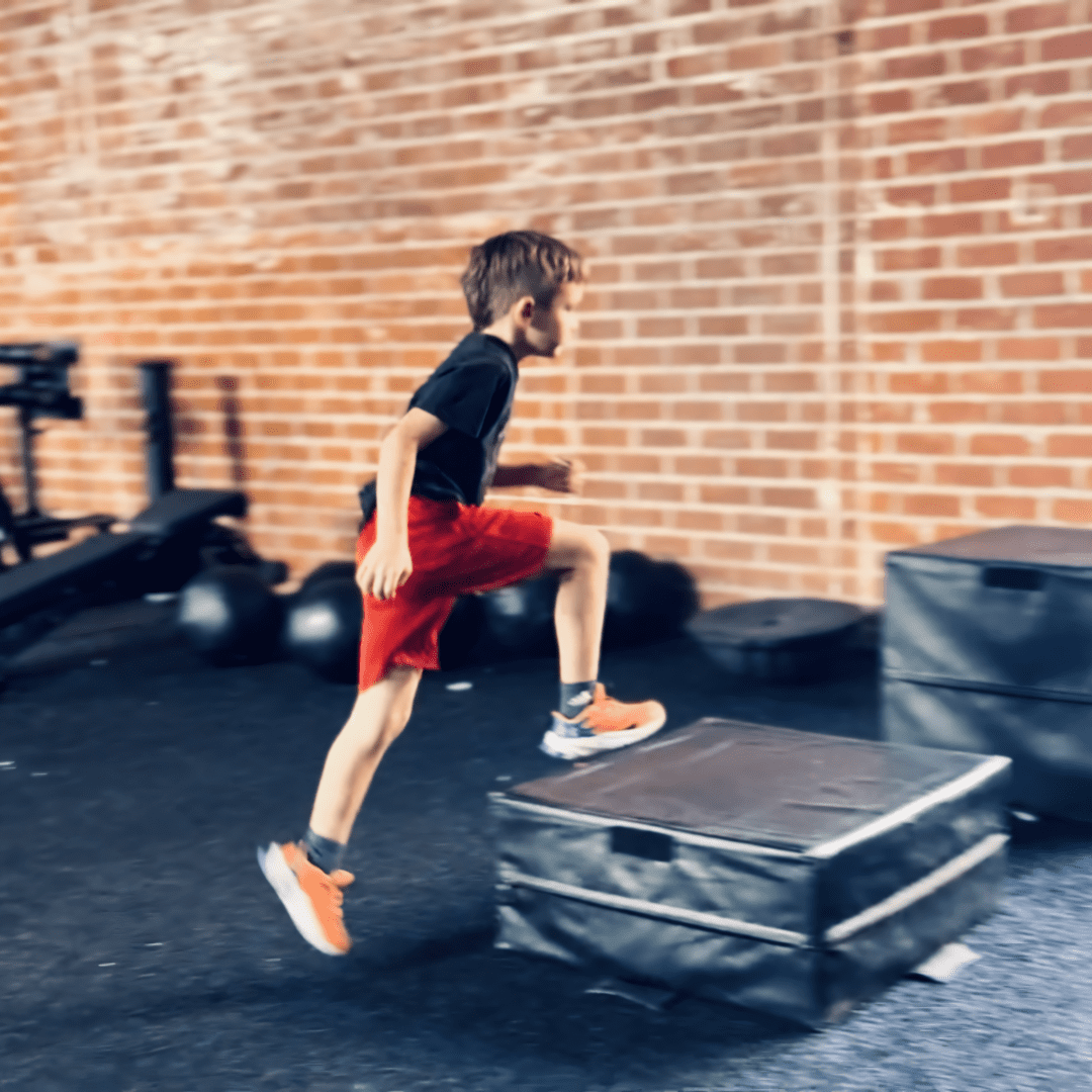 A young man jumping over some boxes in the gym.